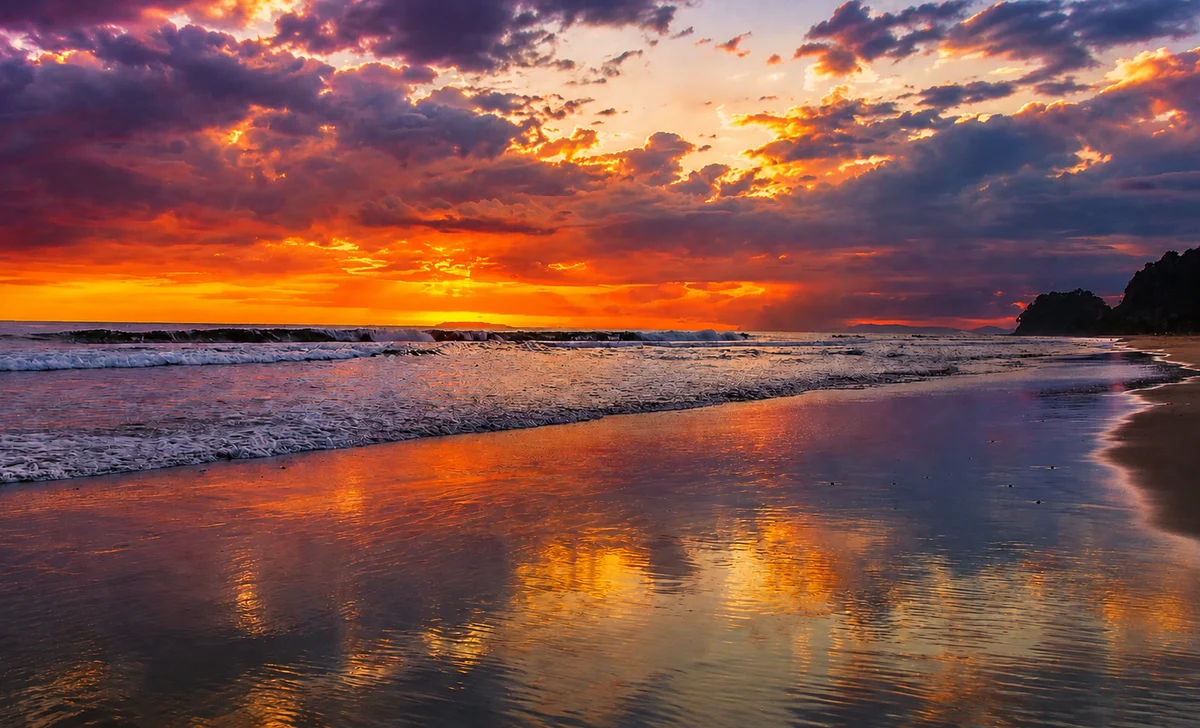 A dramatic orange and purple sunset over the Costa Ballena coastline near Ojochal, Costa Rica, with waves reflecting the colors of the sky