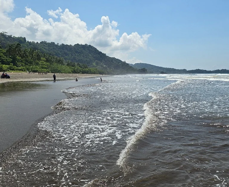 A wide, wild stretch of Playa Hermosa between Uvita and Dominical, Costa Rica, with waves and a jungle-covered mountain backdrop