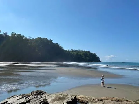 A traveler standing on a quiet Costa Ballena beach near Ojochal under clear blue sky, jungle-covered hills in the background