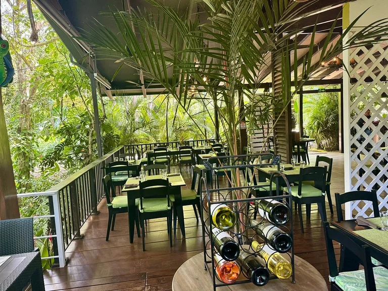 Open-air jungle terrace seating at Heliconia with green cushioned chairs and a wine rack