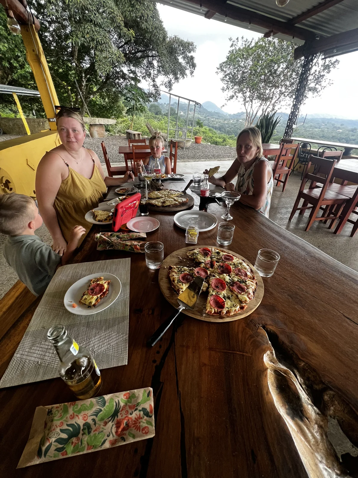 A family sharing wood-fired pizza at an open-air hillside table at La Pala, with mountain views in the background