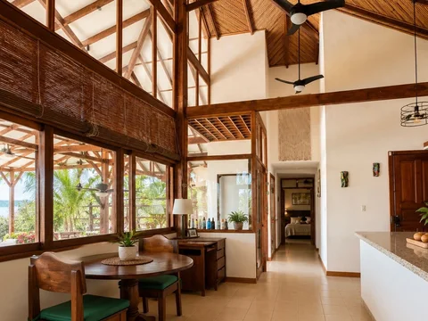 Breakfast nook with a round wood table and green cushioned chairs beneath the villa's vaulted, open-beam ceiling