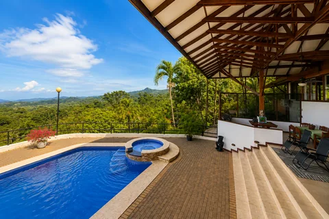 Pool and jacuzzi viewed from under the covered pavilion, with a panoramic jungle and mountain view