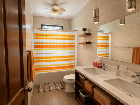 Shared bathroom with a double-sink vanity, tub, and orange striped shower curtain