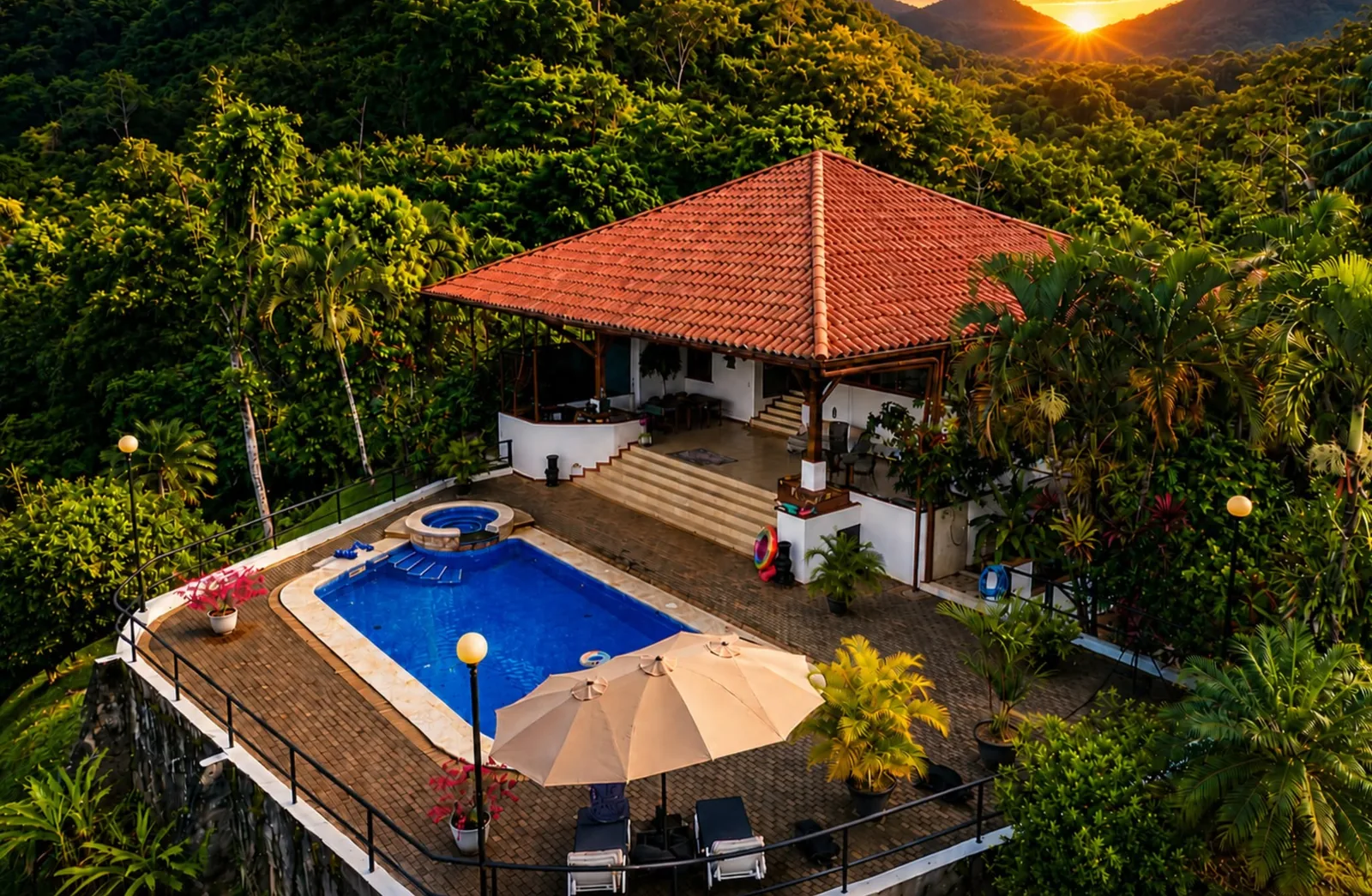 Aerial view of Casa Cascada nestled in the jungle at golden hour, pool and jacuzzi in the foreground with the sun setting between distant mountains